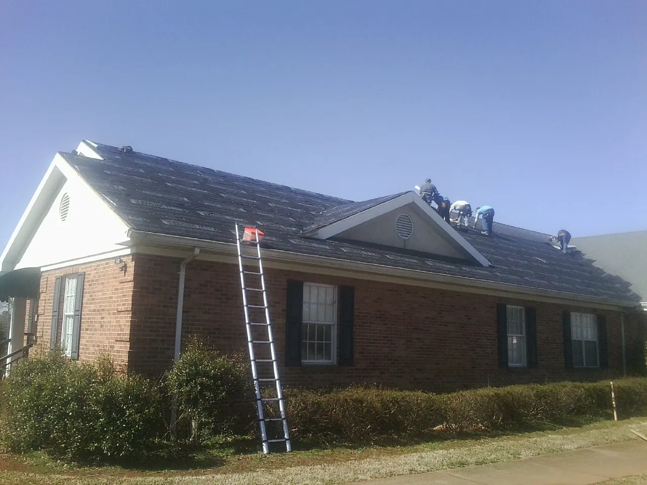 Crew tearing shingles off a brick ranch roof with a ladder set — Emergency Roof Repair work by our crew in Angels Camp