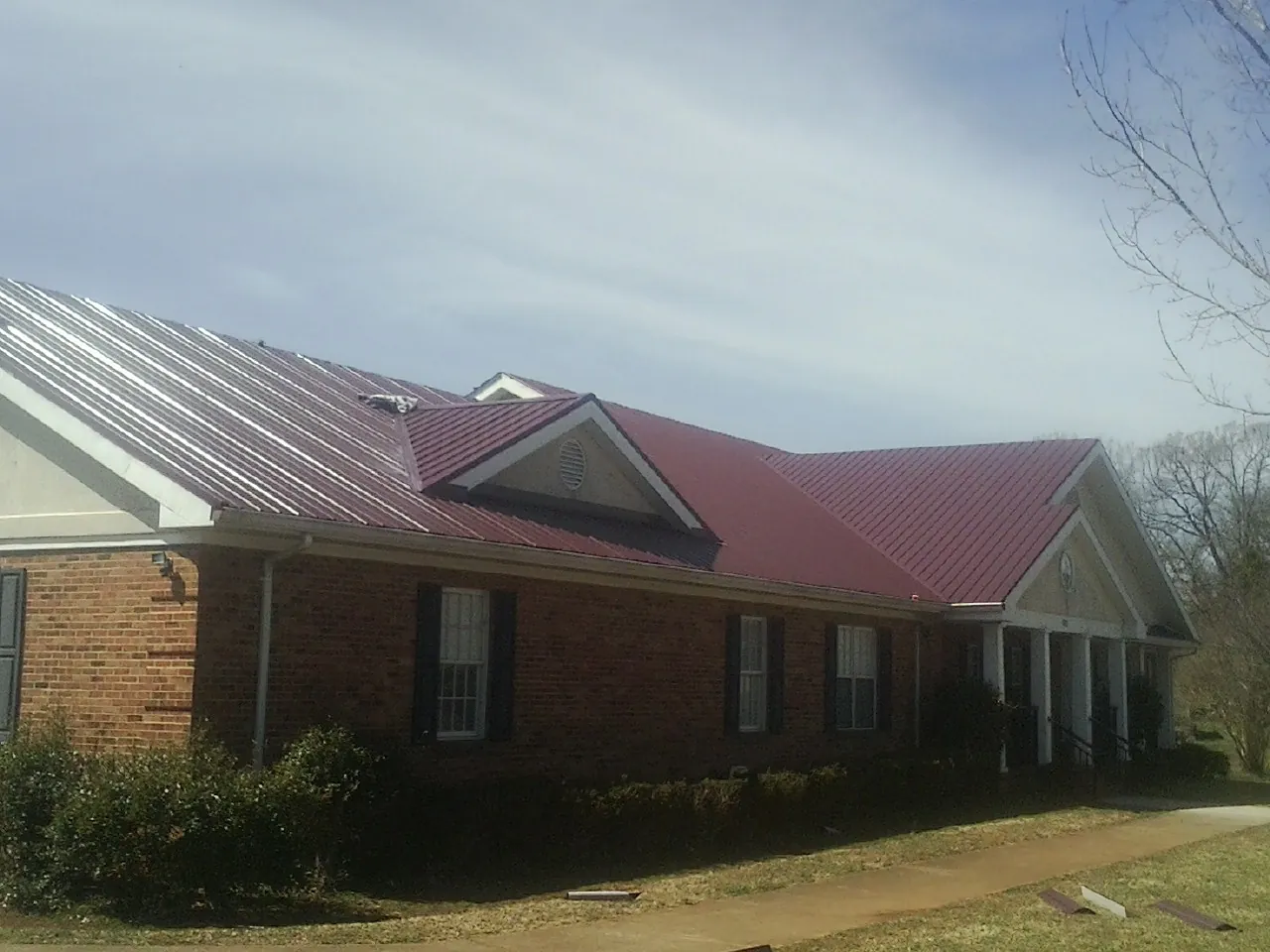 Red metal roof with gabled entries on a long brick building, from a Hail Damage Roof Repair job in Angels Camp