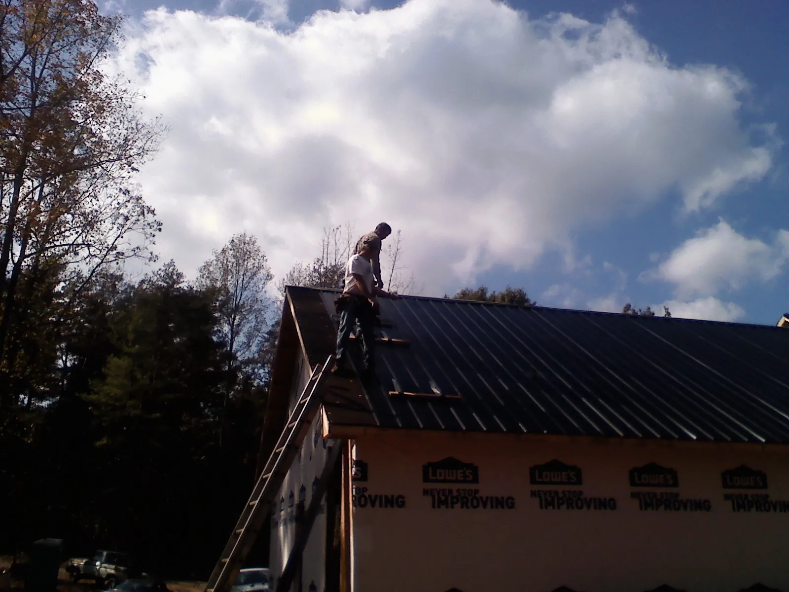 Roofer fastening dark metal panels high against a cloudy sky, from a Roof Inspection job in Angels Camp