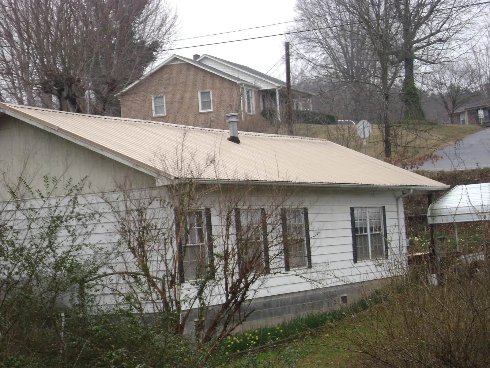 Tan metal roof on a white sided house set into a hillside — Commercial Roofing by Roofing Brothers in Angels Camp